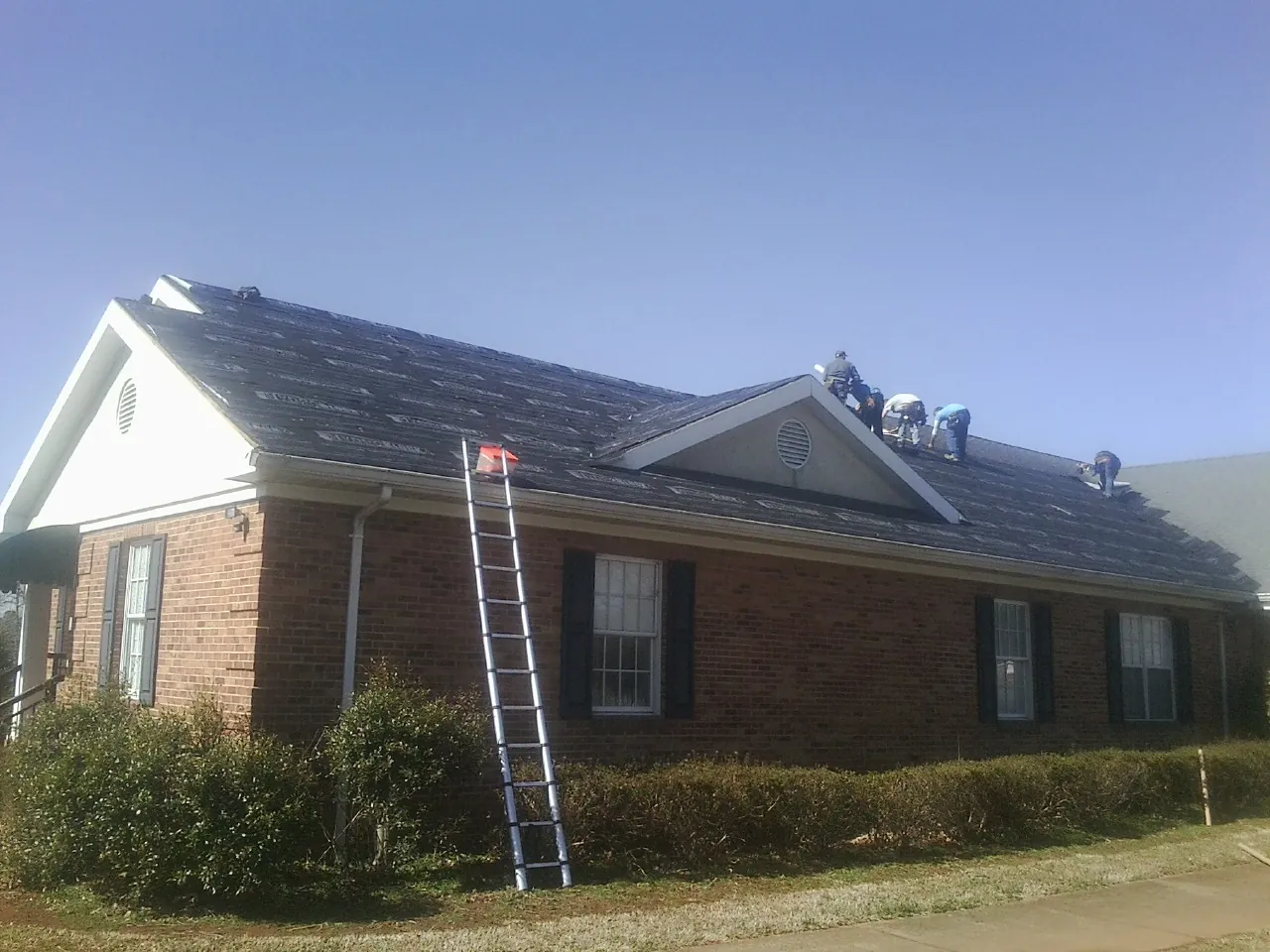 Crew tearing shingles off a brick ranch roof with a ladder set — Emergency Roof Repair work by our crew in Bobtown
