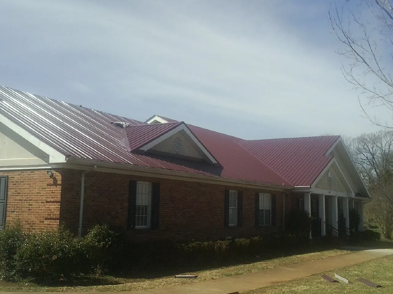 Red metal roof with gabled entries on a long brick building, from a Hail Damage Roof Repair job in Bobtown