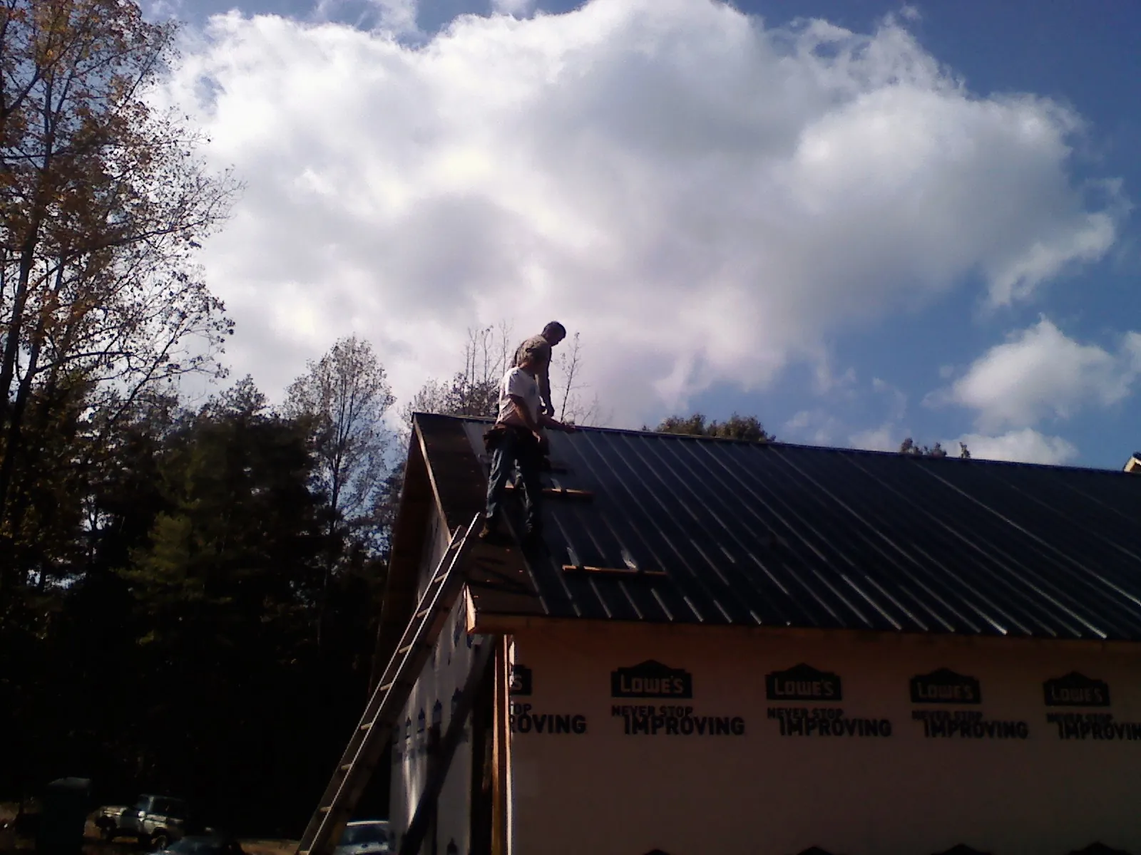 Roofer fastening dark metal panels high against a cloudy sky, from a Roof Inspection job in Bobtown
