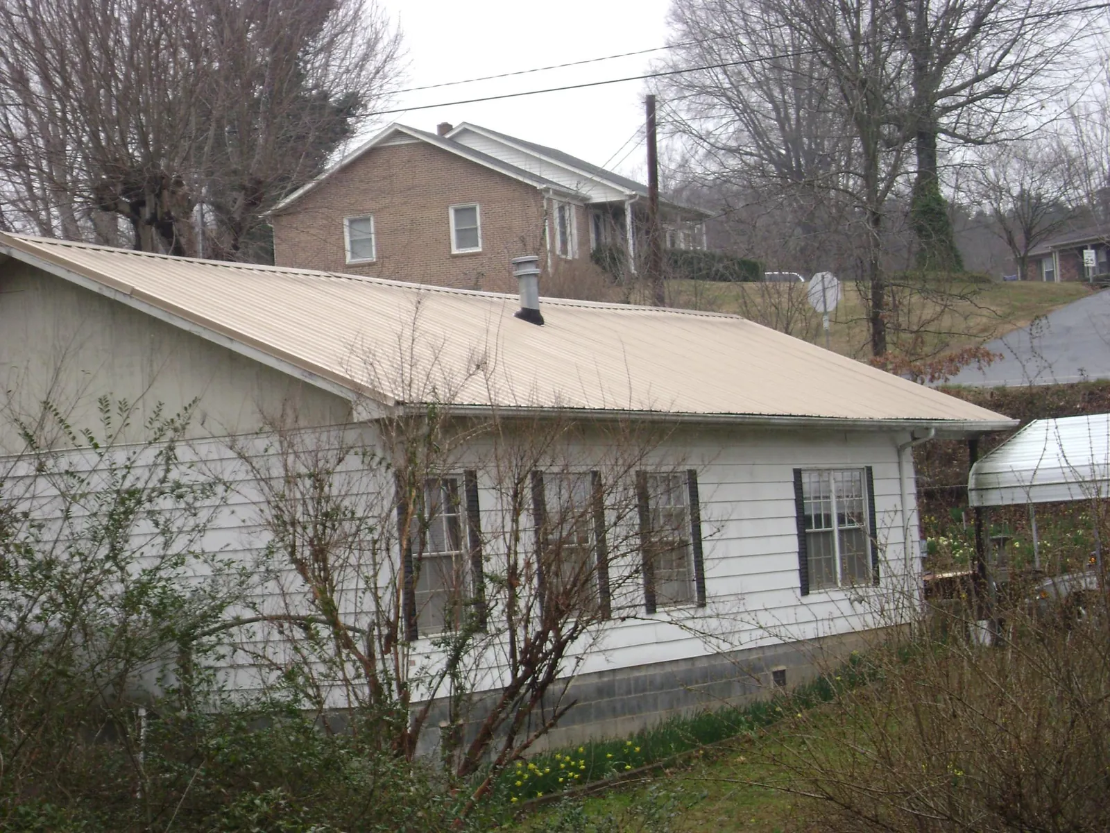 Tan metal roof on a white sided house set into a hillside — Commercial Roofing by Roofing Brothers in Bobtown